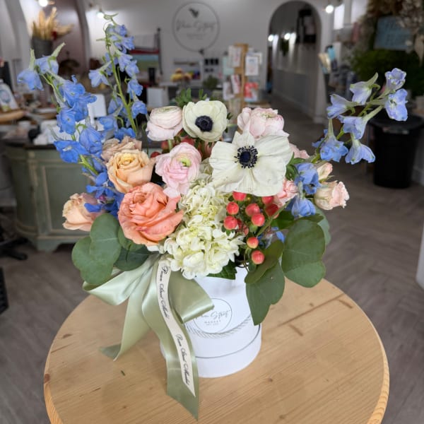 Mixed pastel bouquet in a white hatbox with blue delphinium and roses