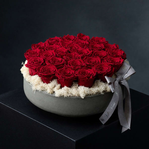 Round box of red roses with a gray ribbon on a dark background