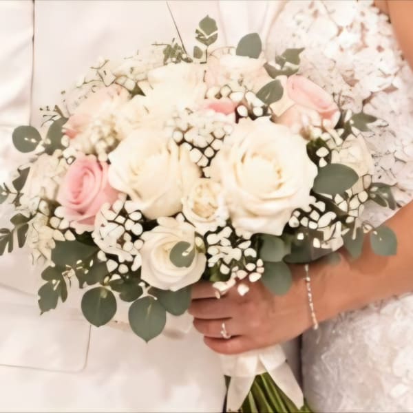 White and blush rose bouquet with eucalyptus held by a bride and groom