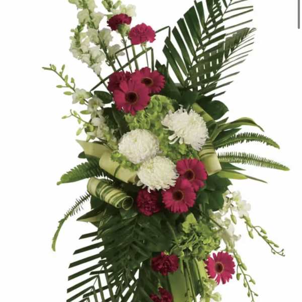 Tall floral spray with pink gerberas, white blooms, and palm fronds on an easel