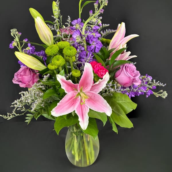 Pink lilies and purple flowers arranged in a clear glass vase
