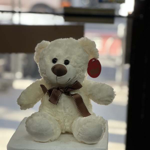 White teddy bear with a brown ribbon sitting on a pedestal