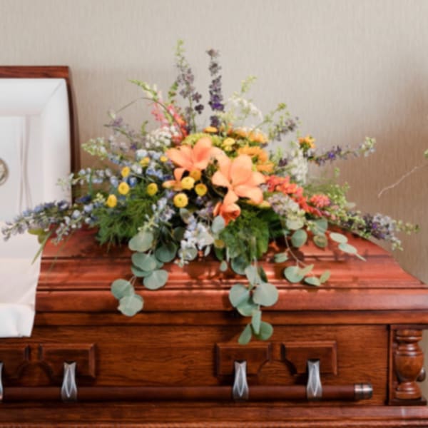 Large floral spray on a wooden casket with peach lilies and mixed blooms