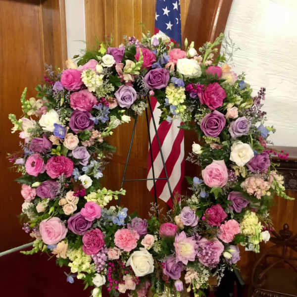 Large floral wreath of pink, purple, and white flowers on a stand
