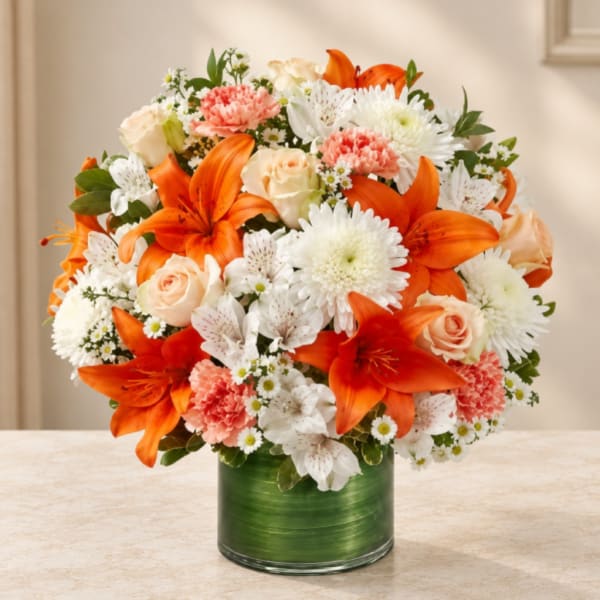 Orange lilies, white chrysanthemums, and peach roses in a green vase