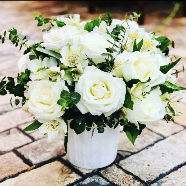 White rose bouquet in a white vase with green foliage