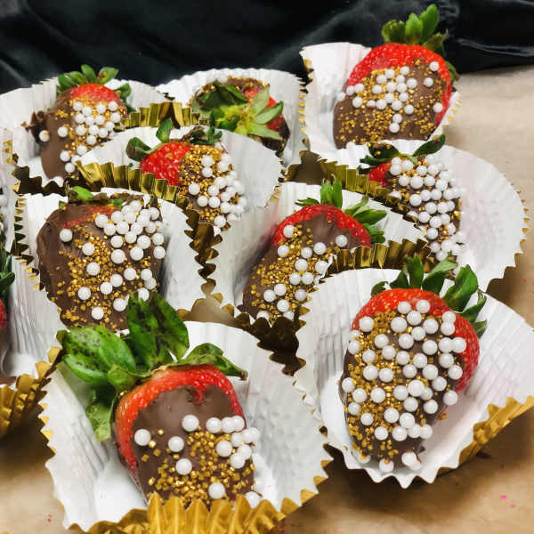 Chocolate-covered strawberries in paper cups with white and gold sprinkles