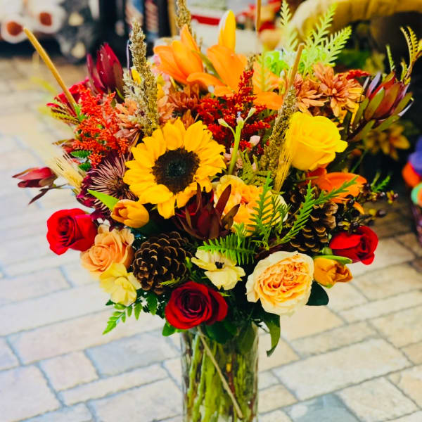 Mixed bouquet with sunflowers, roses, and orange blooms in a glass vase