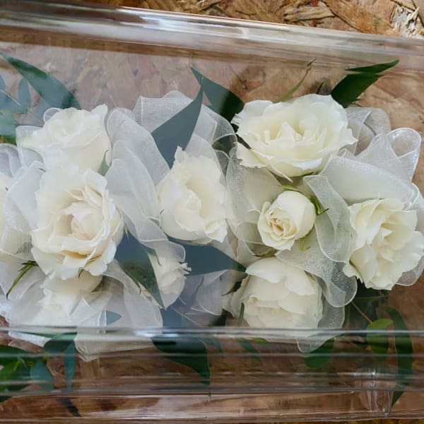 White roses wrapped in sheer fabric inside a clear box