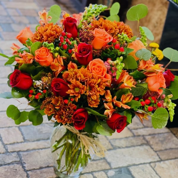 Bouquet of red and orange roses with orange chrysanthemums in a glass vase