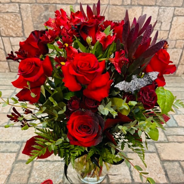 Red rose bouquet in a clear glass vase with mixed greenery