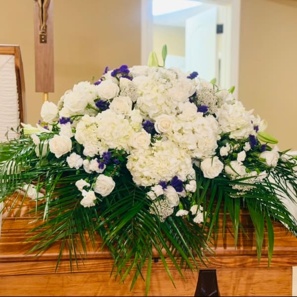 White floral casket spray with purple accents and palm fronds