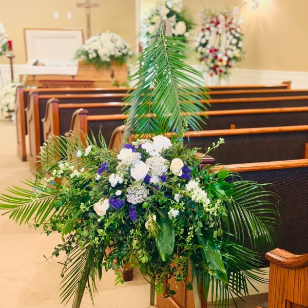 Large floral arrangement with white roses and greenery in a church pew