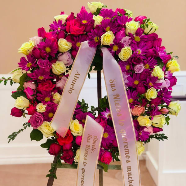 Large floral wreath of pink, purple, and cream roses with ribbon streamers
