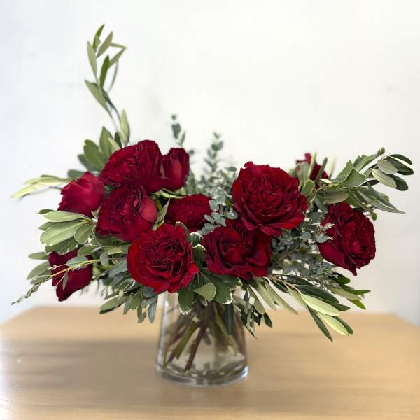 Red roses arranged in a clear glass vase with greenery