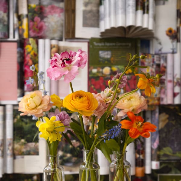 Three small glass vases hold colorful mixed flowers on a stone pedestal.