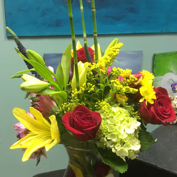 Mixed bouquet of roses, lilies, hydrangea, and daisies in a glass vase