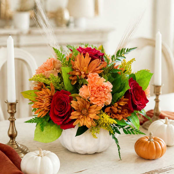 Autumn floral arrangement in a white pumpkin vase with red roses and orange blooms