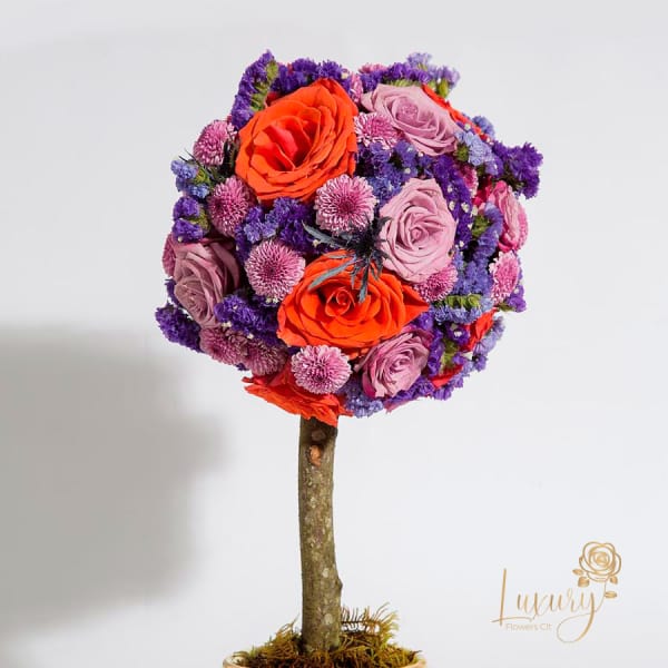 Round bouquet of orange and lavender roses with purple filler flowers on a stem
