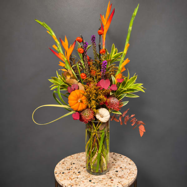 Tropical floral arrangement in a tall glass vase with orange and purple accents