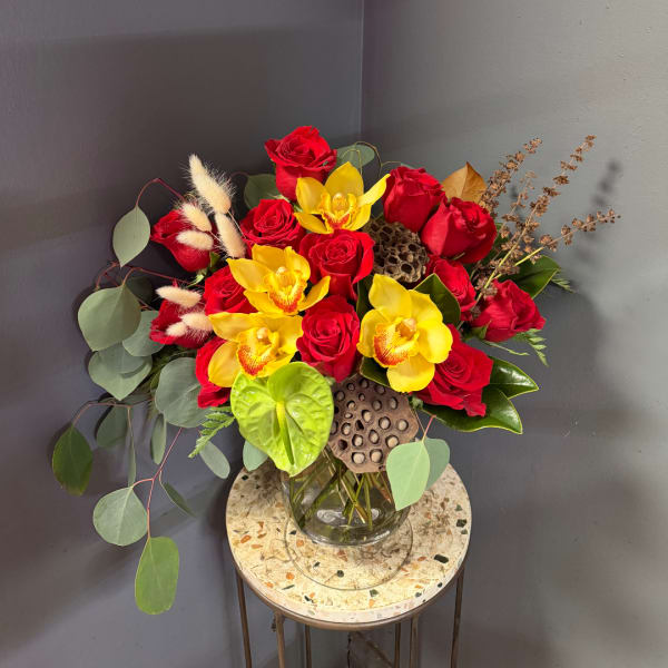 Red roses and yellow orchids arranged in a glass vase