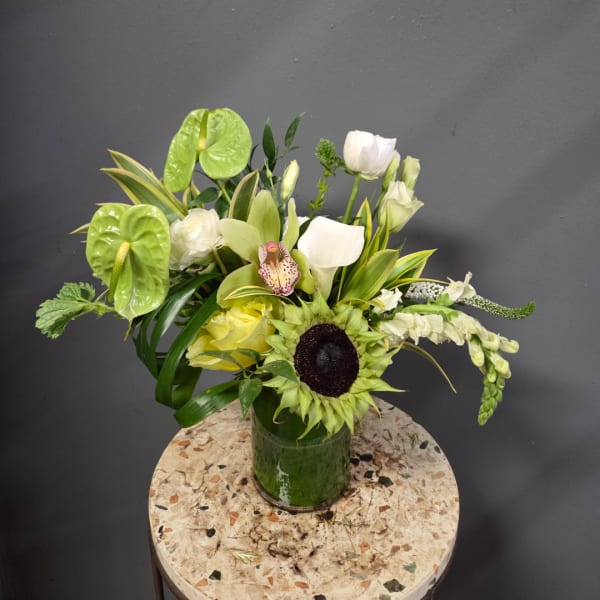 Mixed floral arrangement in a green glass vase with white and green blooms