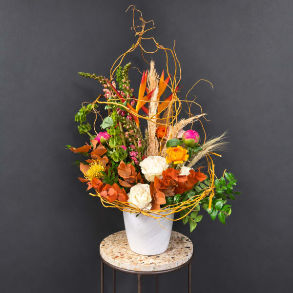 Tall floral arrangement with orange, pink, and white blooms in a white vase