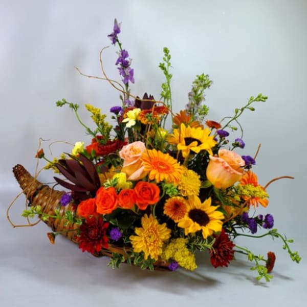 Mixed bouquet in a woven basket with sunflowers, roses, and orange blooms