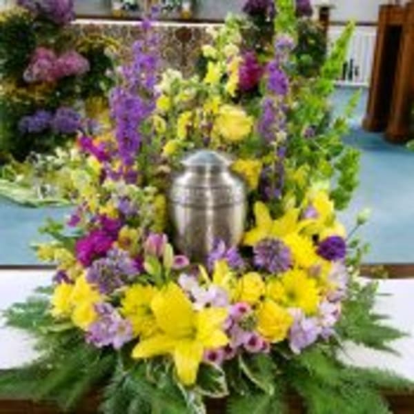Ring of yellow and purple flowers surrounding a silver cremation urn