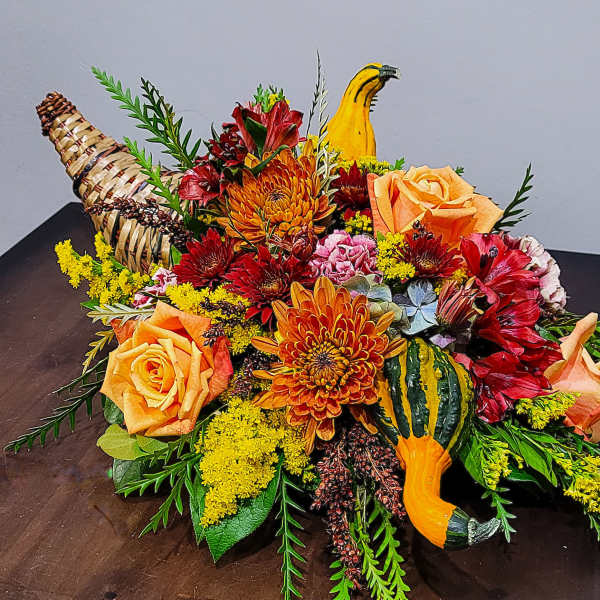 Autumn centerpiece with orange roses, mums, red flowers and gourds in a woven cornucopia