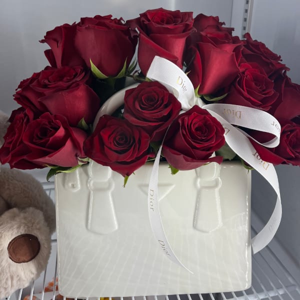 Red roses arranged in a white ceramic vase with a ribbon bow