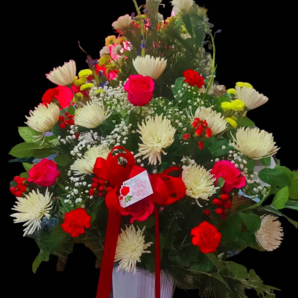 Large mixed flower arrangement in a white vase with a red ribbon