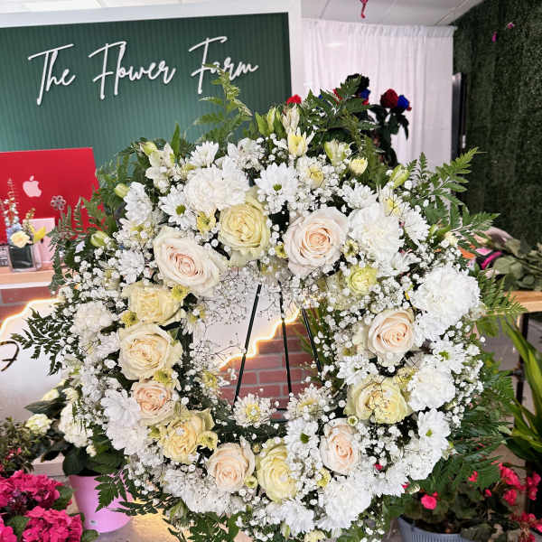 Large white floral wreath on a stand with cream roses and daisies
