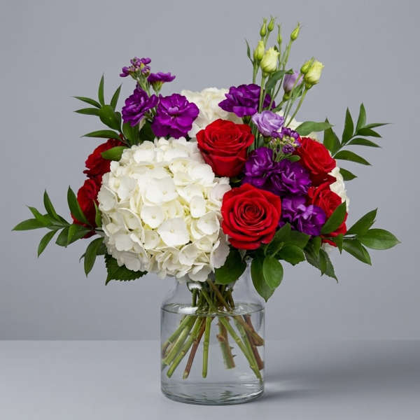 Bouquet of red roses, white hydrangeas, and purple flowers in a glass vase