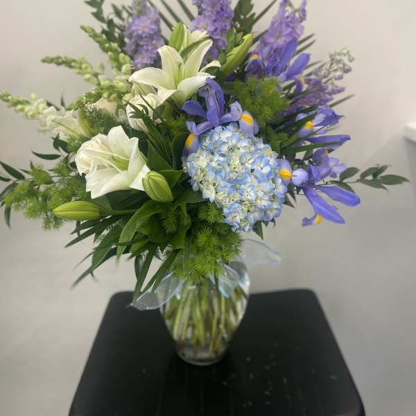 White lilies and blue-purple flowers in a glass vase