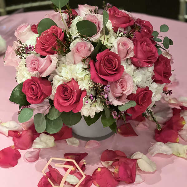Pink and white rose arrangement in a white vase on a pink table