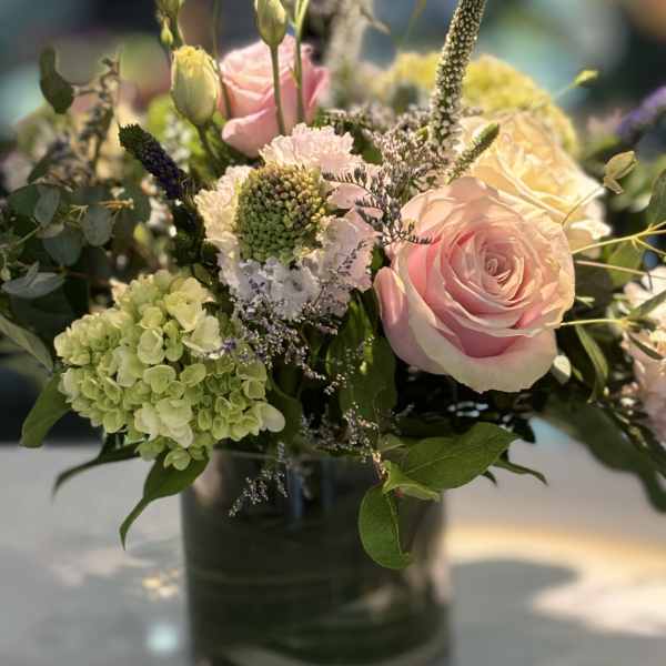 Arrangement of pink roses, green hydrangeas, and mixed blooms in a clear glass vase