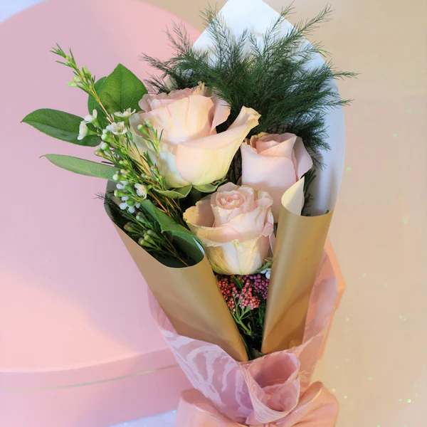 Bouquet of pale pink roses wrapped in gold paper with a pink ribbon