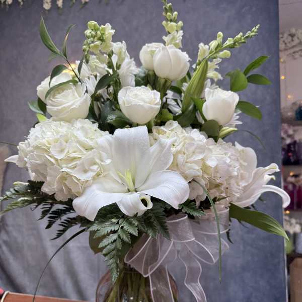 White lilies, roses, and hydrangeas in a glass vase with a sheer ribbon