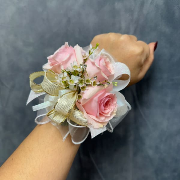 Pink rose wrist corsage with white ribbon and gold bow on a wrist