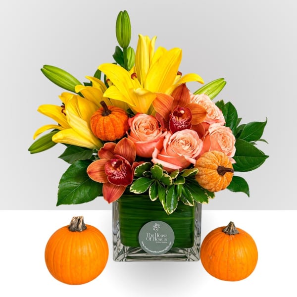 Yellow lilies and peach roses in a glass vase with small pumpkins