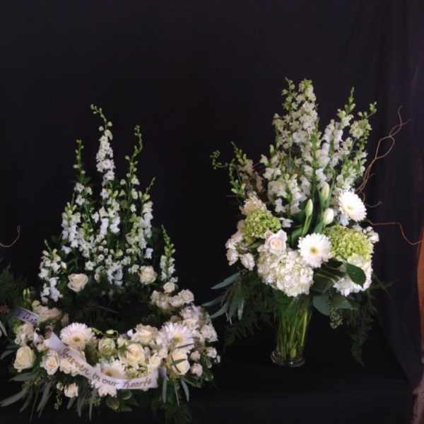Three white floral funeral arrangements with a memorial ribbon