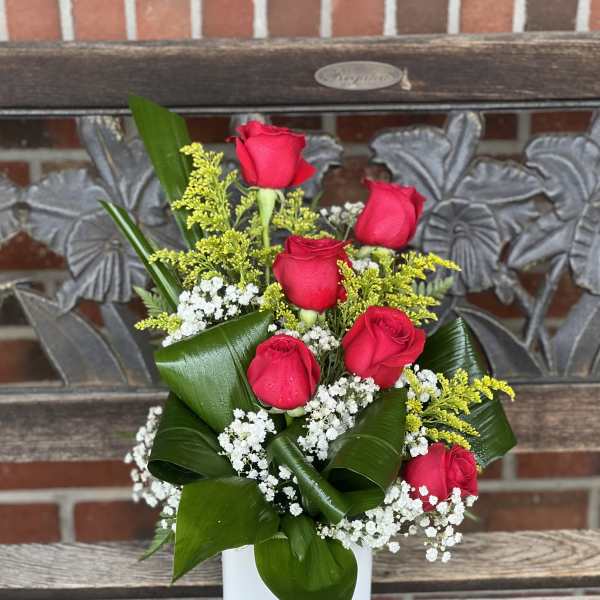 Red roses arranged in a white vase with baby's breath and greenery