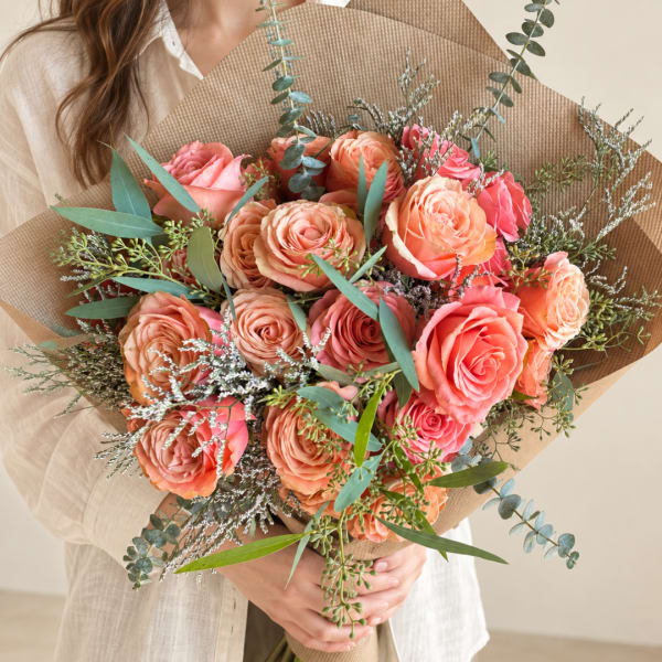 Handheld bouquet of peach and pink roses wrapped in brown paper