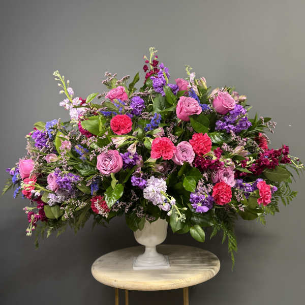 Large mixed bouquet of pink, purple, and red flowers in a white urn vase
