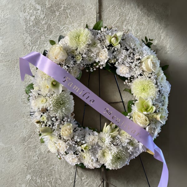 White floral wreath on a stand with a lavender ribbon