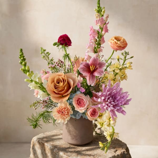 Mixed bouquet in a taupe vase with pink, peach, purple, and white flowers