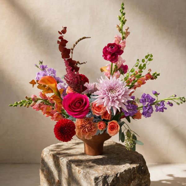 Colorful mixed flower arrangement in a brown vase on a stone pedestal