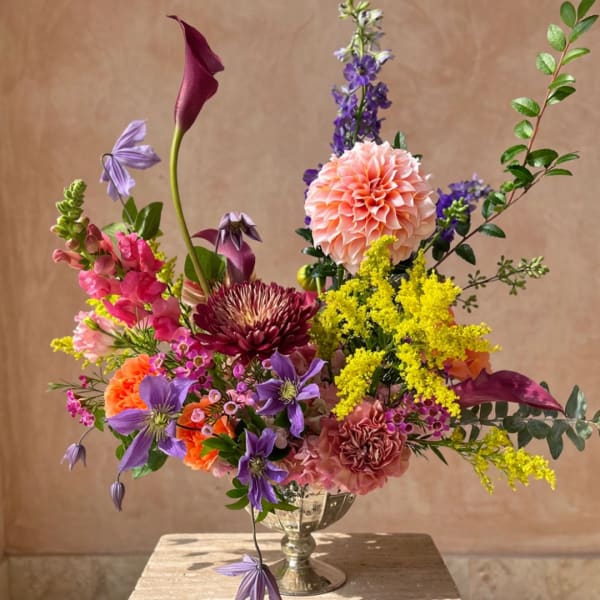 Colorful mixed bouquet in a silver vase with purple, pink, yellow, and peach blooms