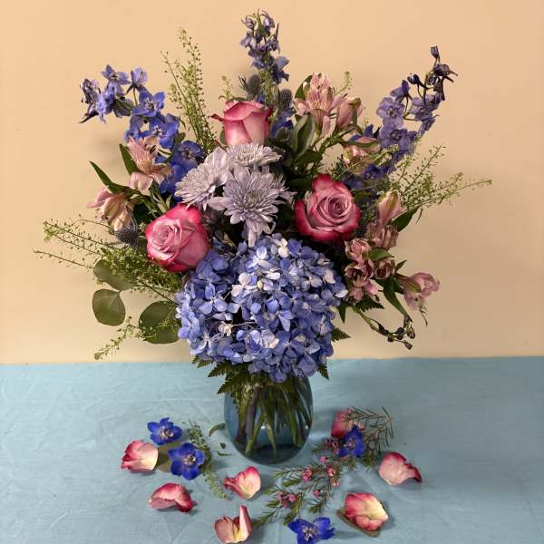 Blue and pink mixed bouquet in a glass vase with scattered petals